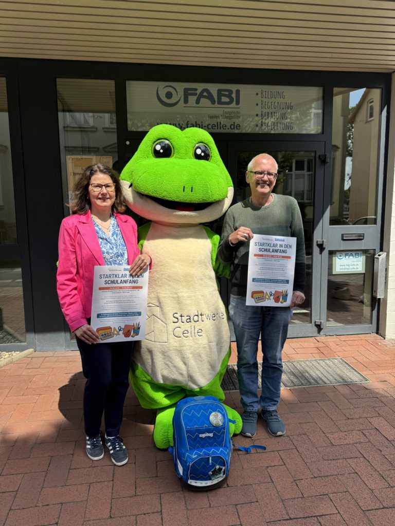Eine Dame und ein Mann halten ein Info-Plakat des Projekts "Startklar" in den Händen. In der Mitte steht das Maskottchen der Stadtwerke Celle "Fiete" (ein Frosch).