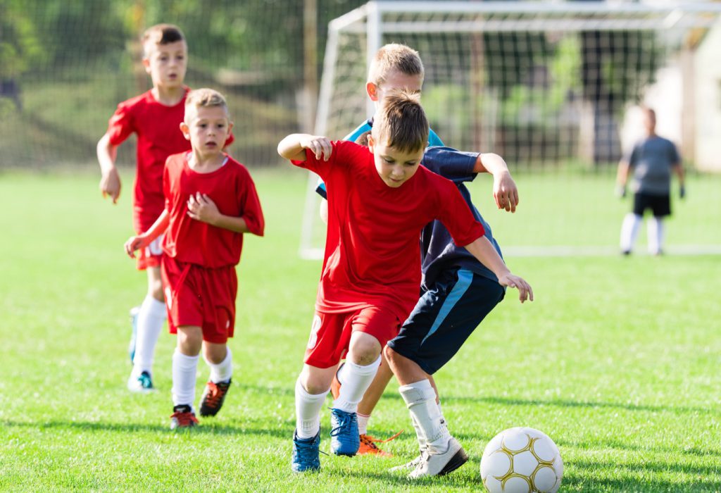 Szene eines Fußballspiels: Zwei Jungs aus gegnerischen Mannschaften versuchen den Ball zu erreichen. Von hinten kommen weitere Jungs angelaufen.